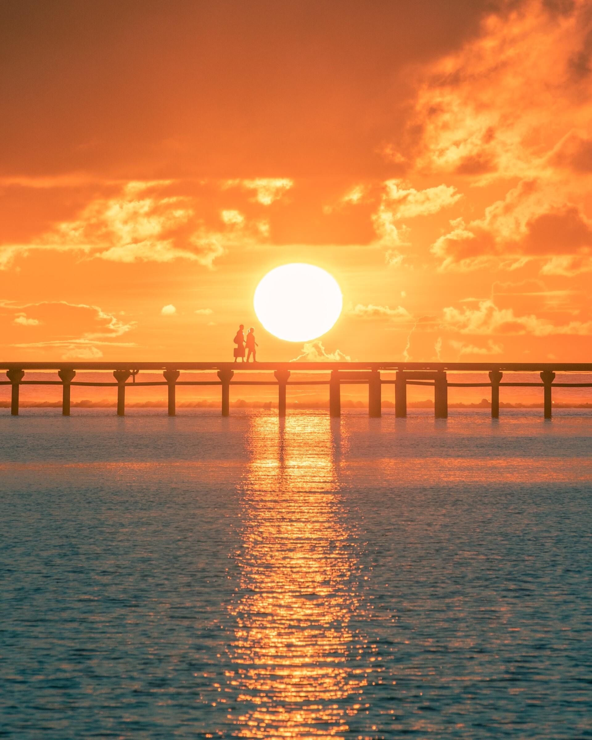 Sunset over the ocean with a pier silhouetted against an orange sky and reflected light on the water