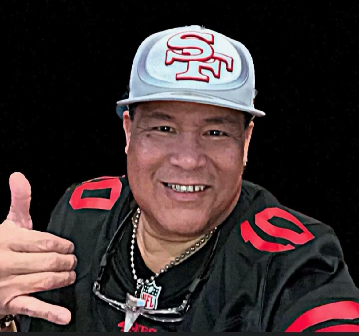 Smiling man in a black sports jersey and gray cap gives a thumbs-up on a black background