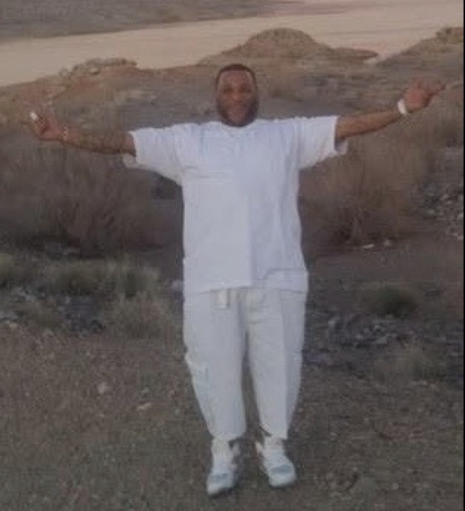 Person in white clothes standing outdoors with arms outstretched in a rocky, sandy landscape.
