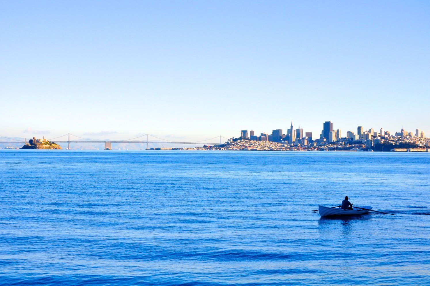 Rowboat on calm blue water with a city skyline in the distance