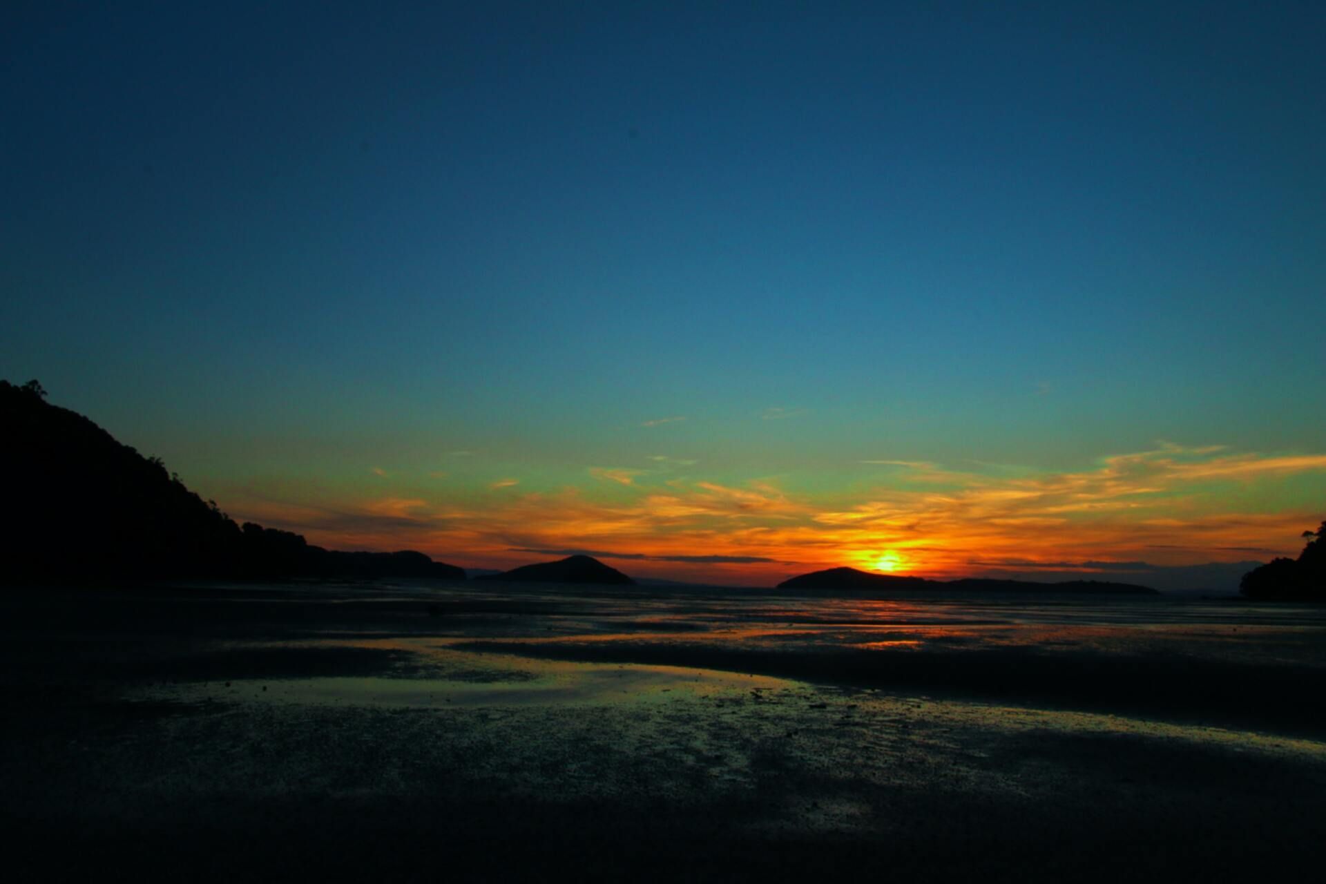 Sunset over a calm bay with silhouetted hills and a glowing orange horizon