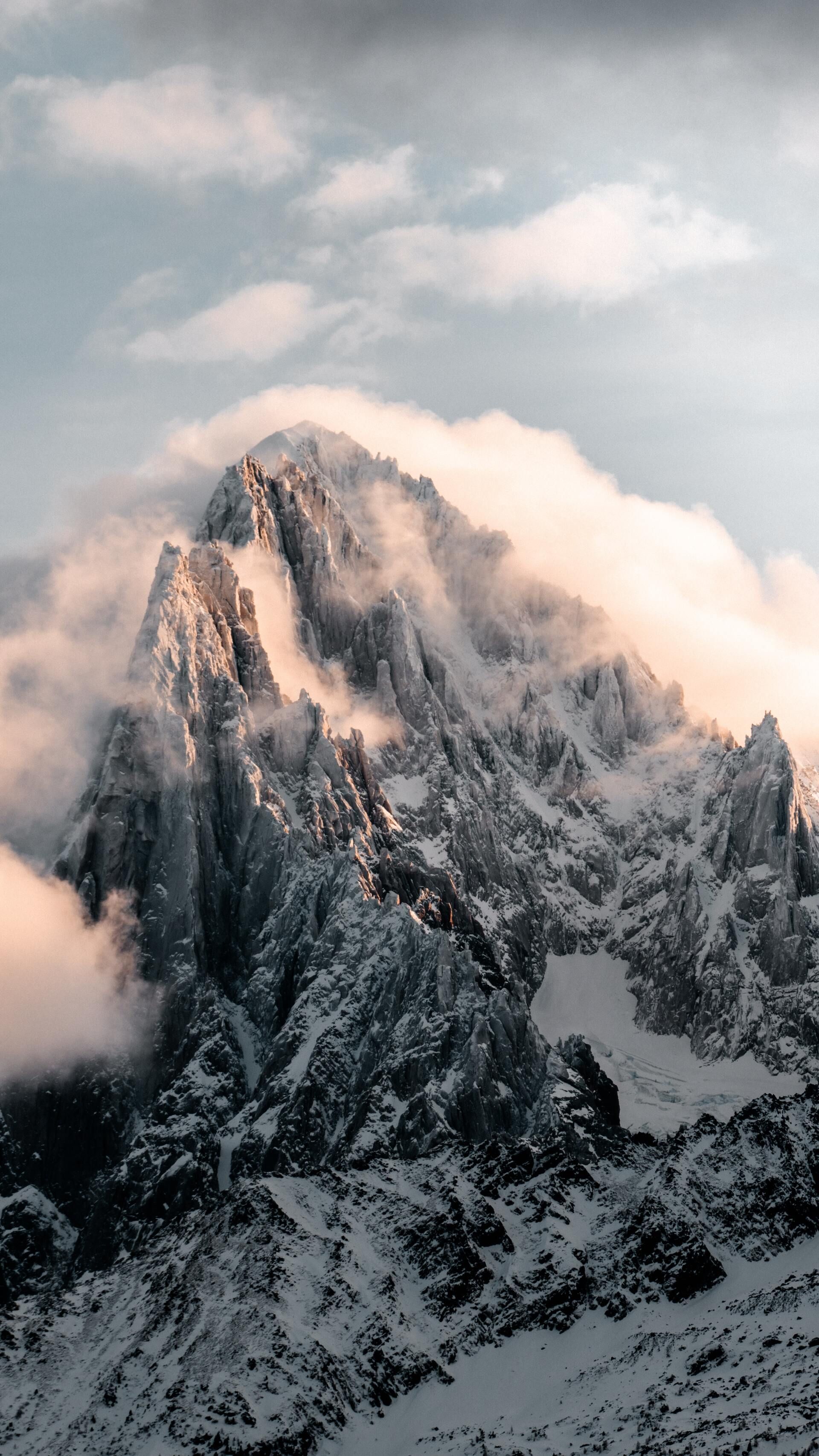 Snow-covered mountain peak rising through clouds at sunrise