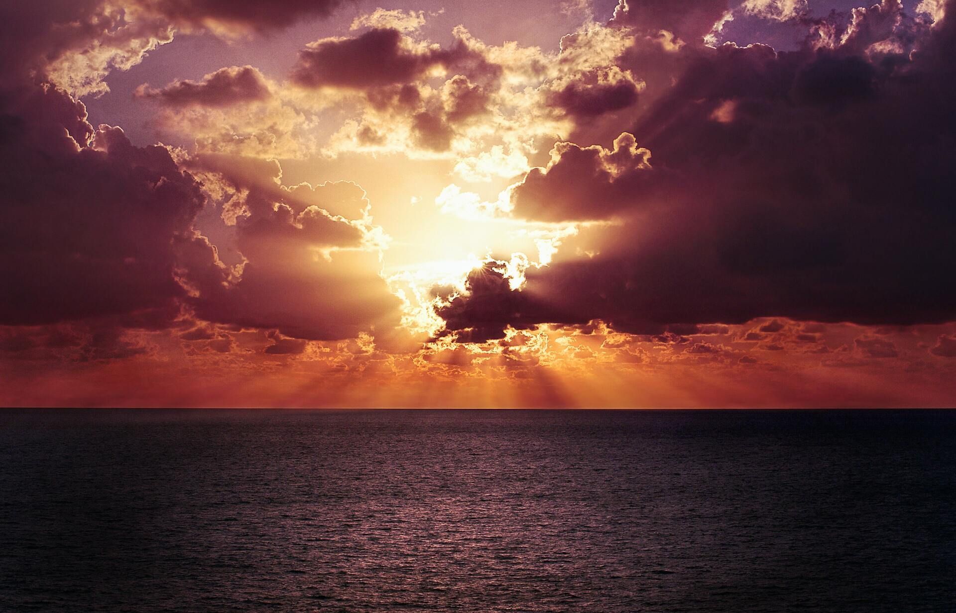 Sunset over the ocean with dramatic clouds and golden light reflecting on dark water