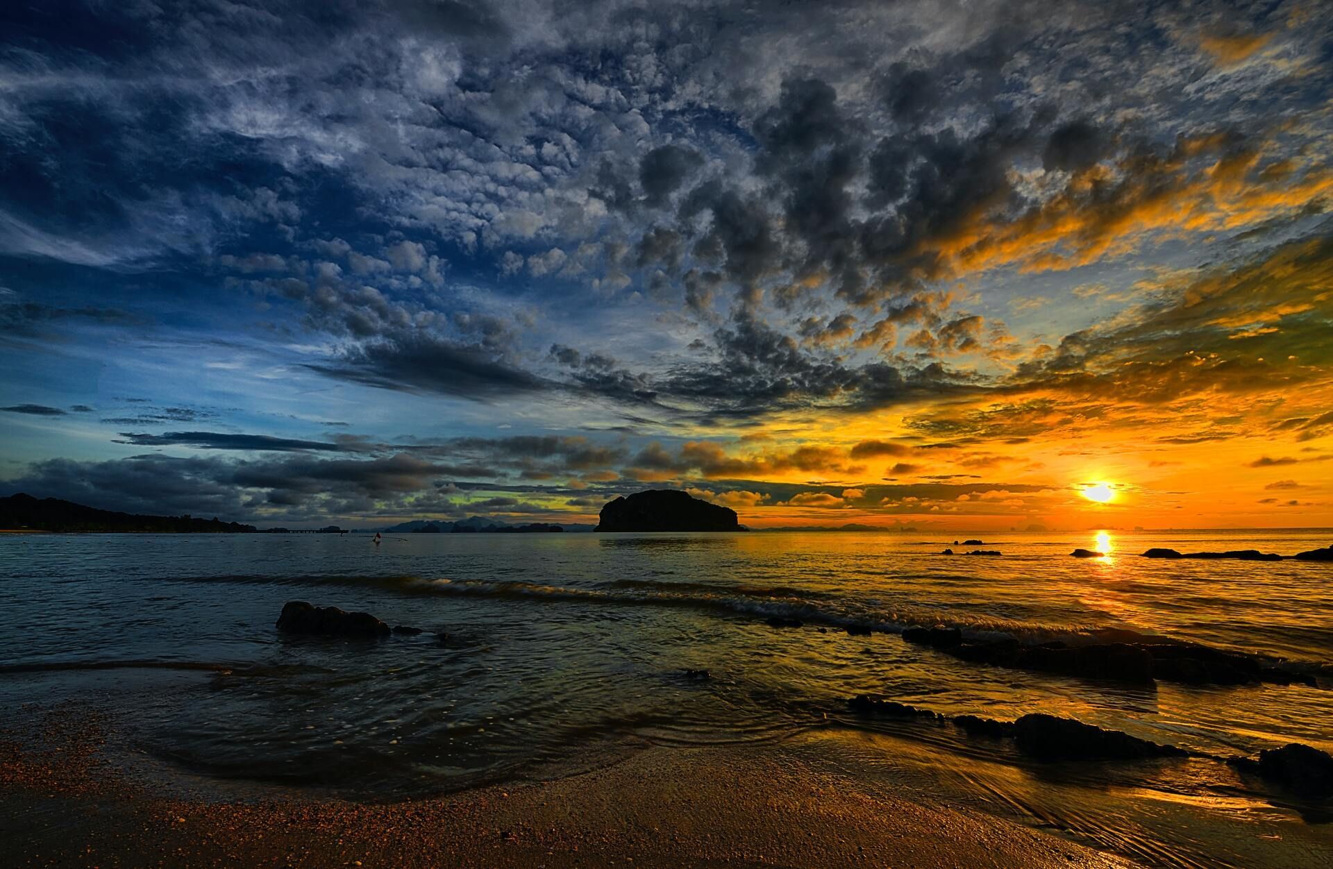 Sunset over a rocky beach with dramatic clouds and the sun near the horizon.