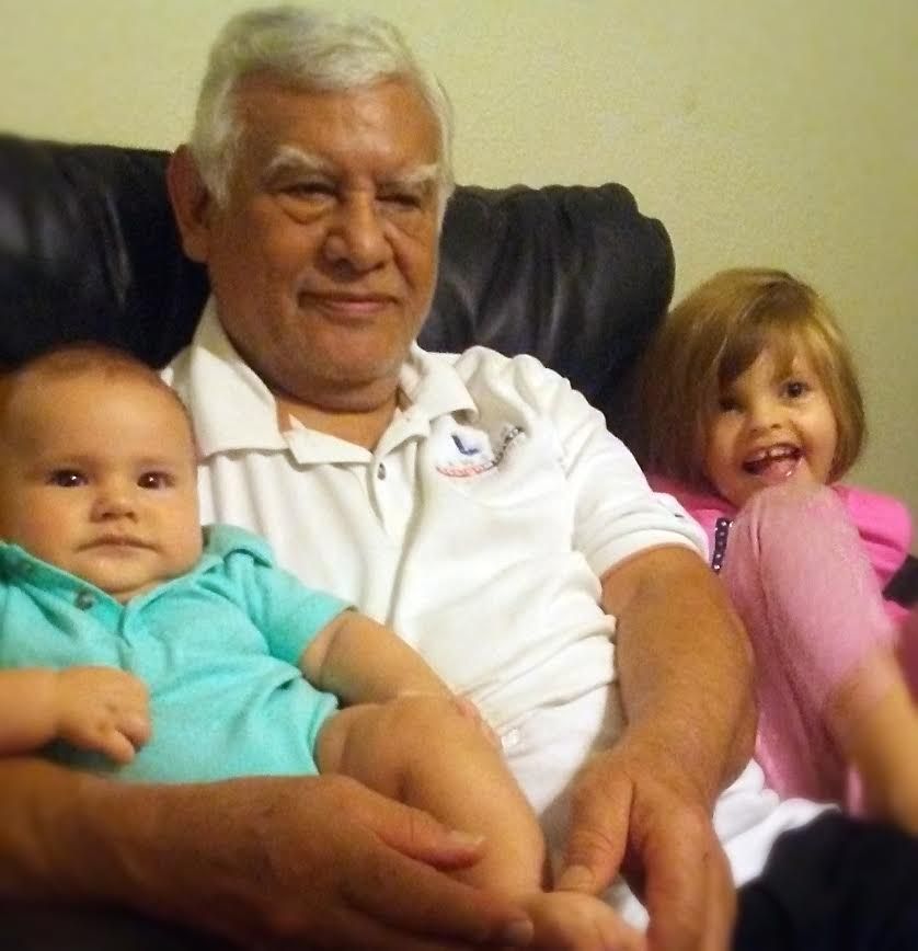 Older man sitting on a couch with two young children, one in turquoise and one in pink, both facing the camera