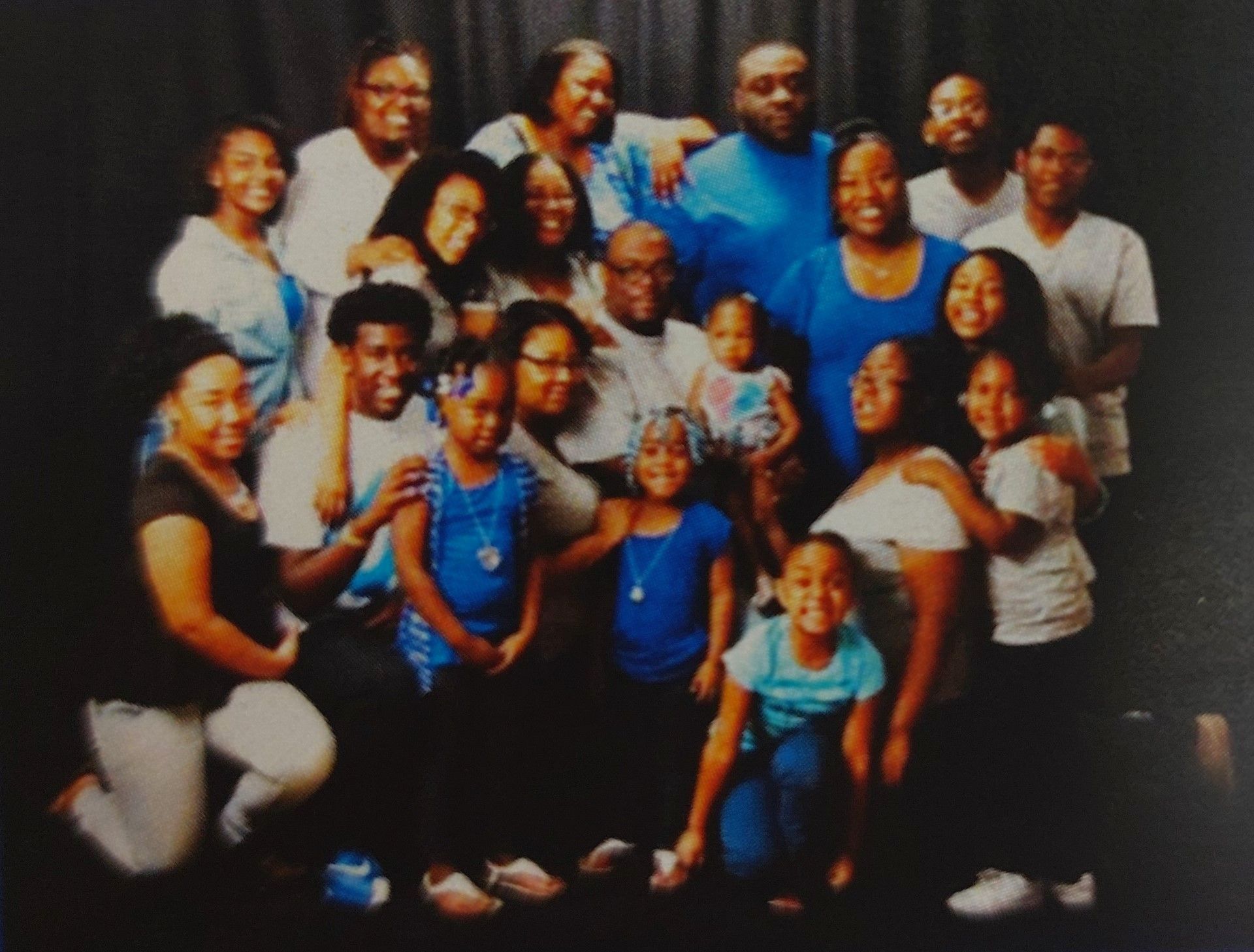 Group of smiling people posing together in matching blue and white shirts against a dark background
