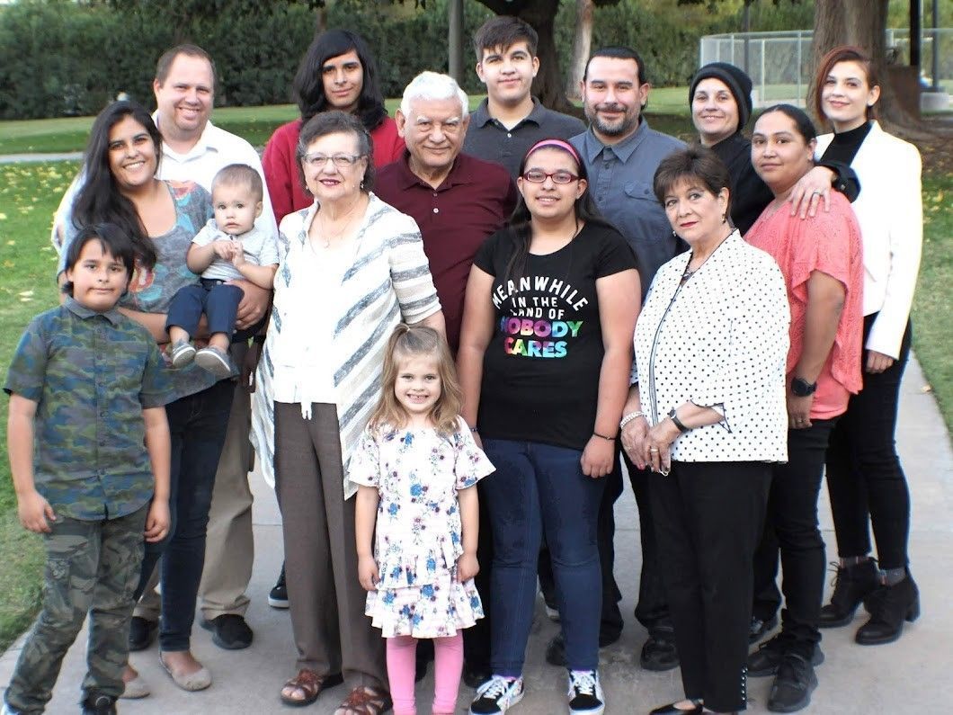 Large group posing outdoors, with adults and children standing closely together in casual clothes.