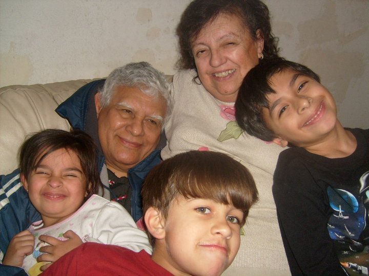 Five smiling people sitting closely together on a couch indoors