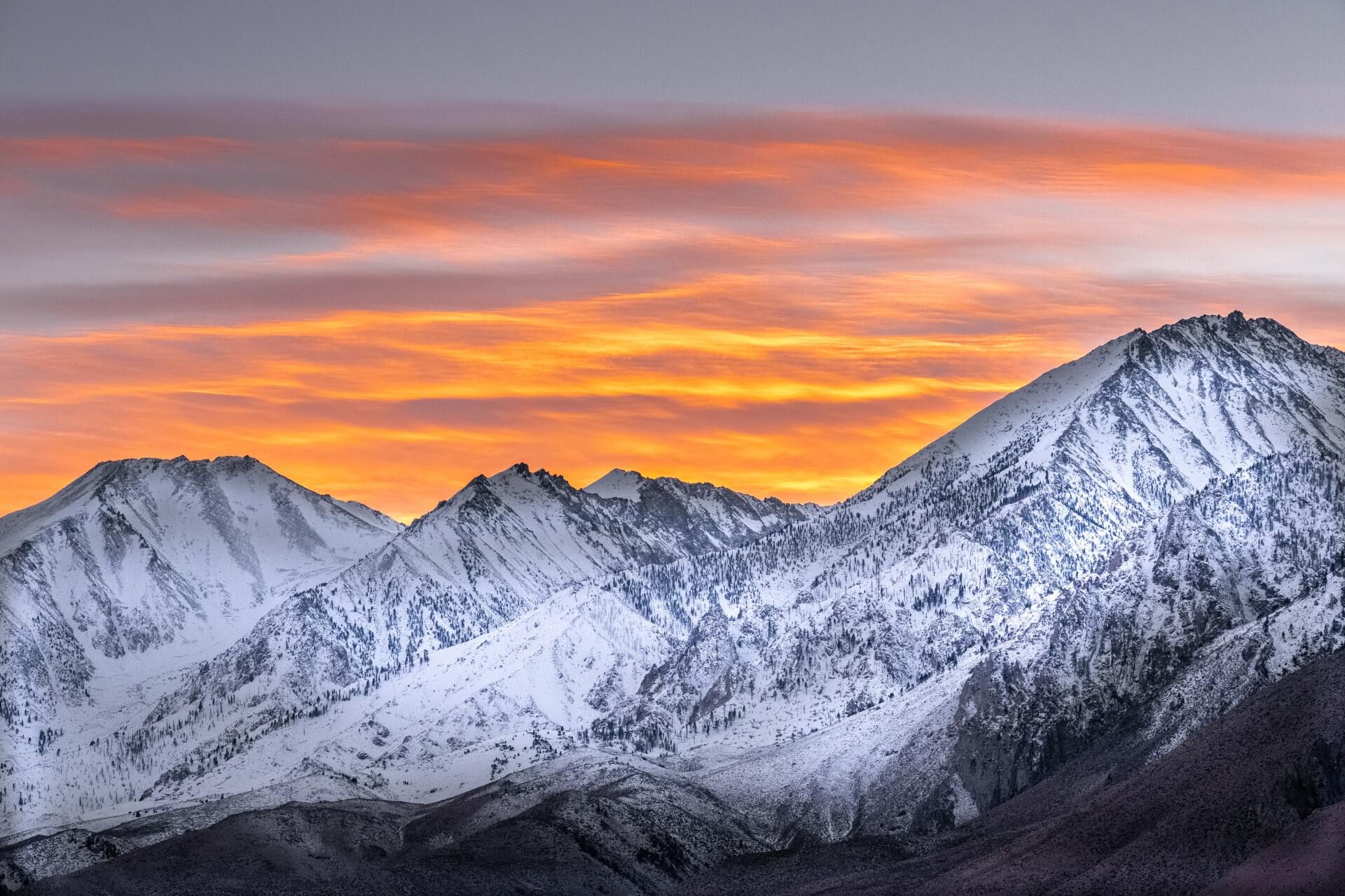 Snow-covered mountains at sunset with orange and pink clouds in the sky