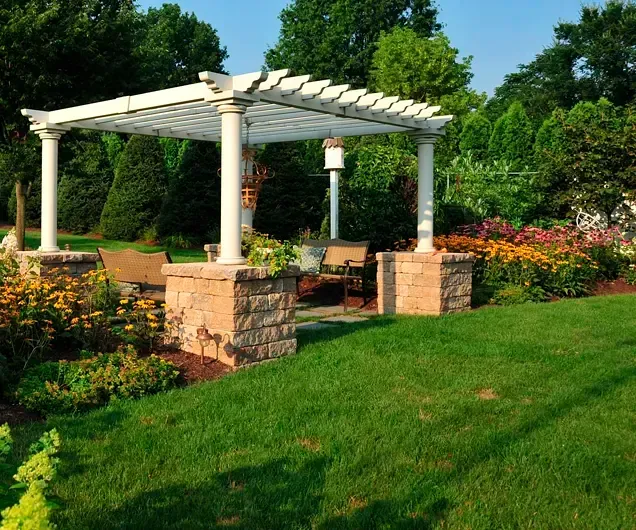 A white pergola is sitting in the middle of a lush green garden.