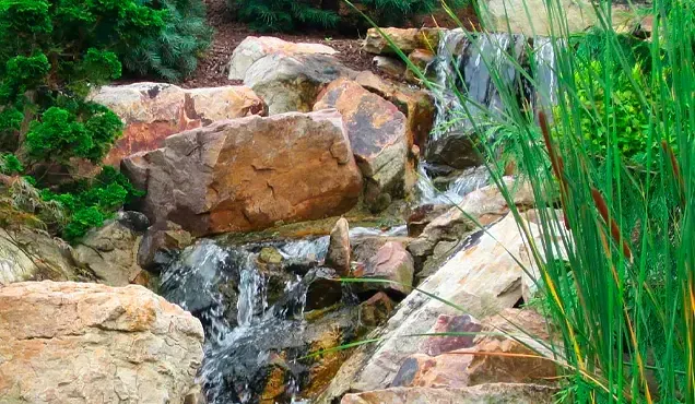 A small waterfall is surrounded by rocks and grass in a garden.