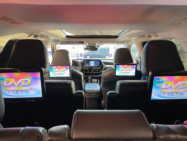 Interior of a car with multiple DVD screens on the seats and dashboard, viewed from the back seat