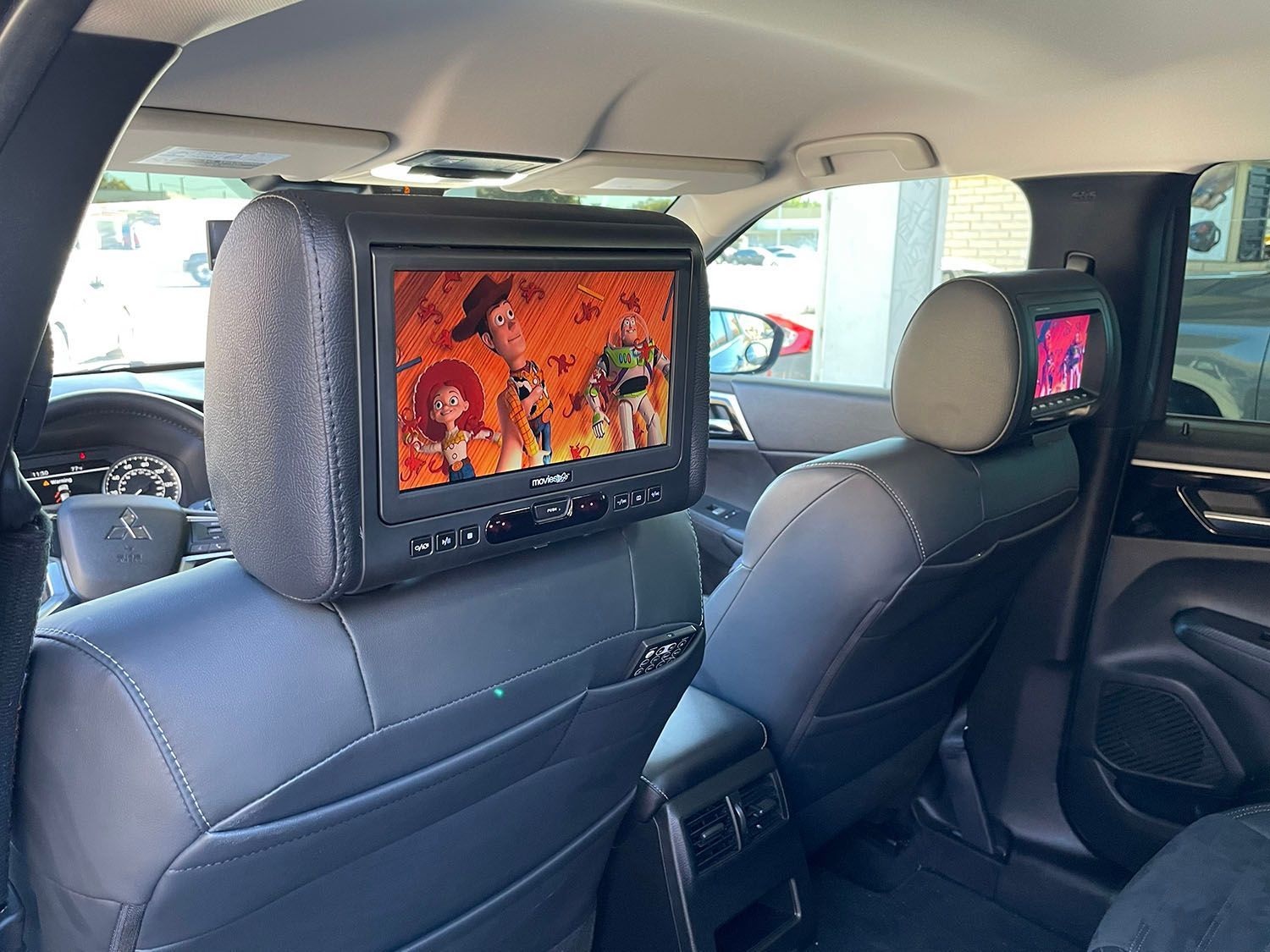 Car interior with two rear-seat entertainment screens showing an animated movie