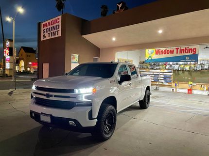 White pickup truck parked outside a tint shop at night with illuminated storefront signs.