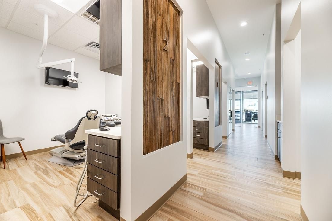 Dental office interior: hallway with wood-look flooring and cabinets. Dental chair in the treatment room.