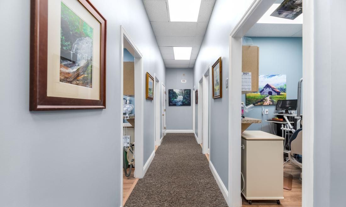 Long hallway with light blue walls, brown carpet, and open doorways to offices; artwork on walls.