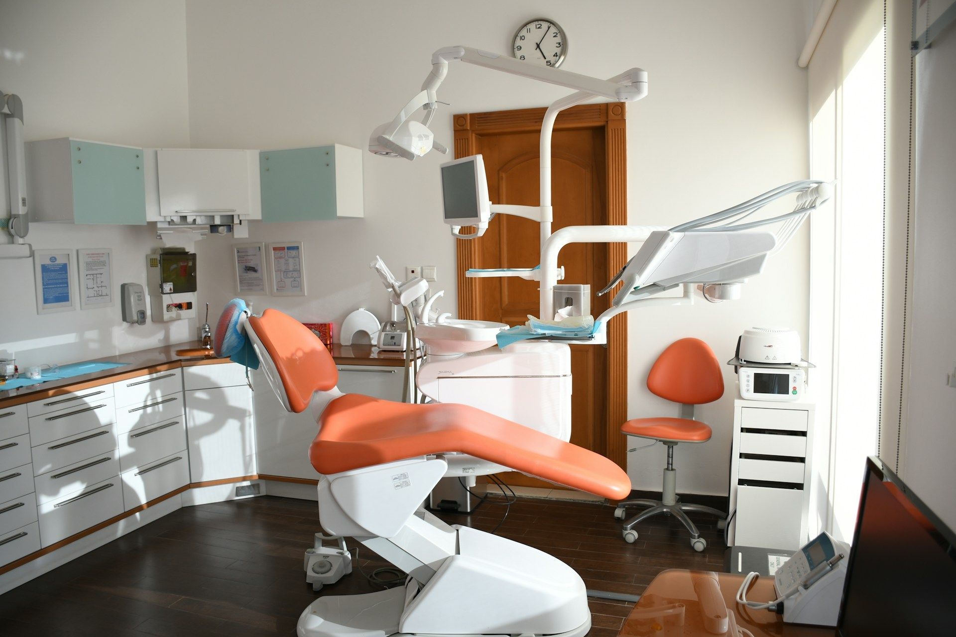 Dental examination room with orange chair and cabinets, medical equipment, and a small stool.