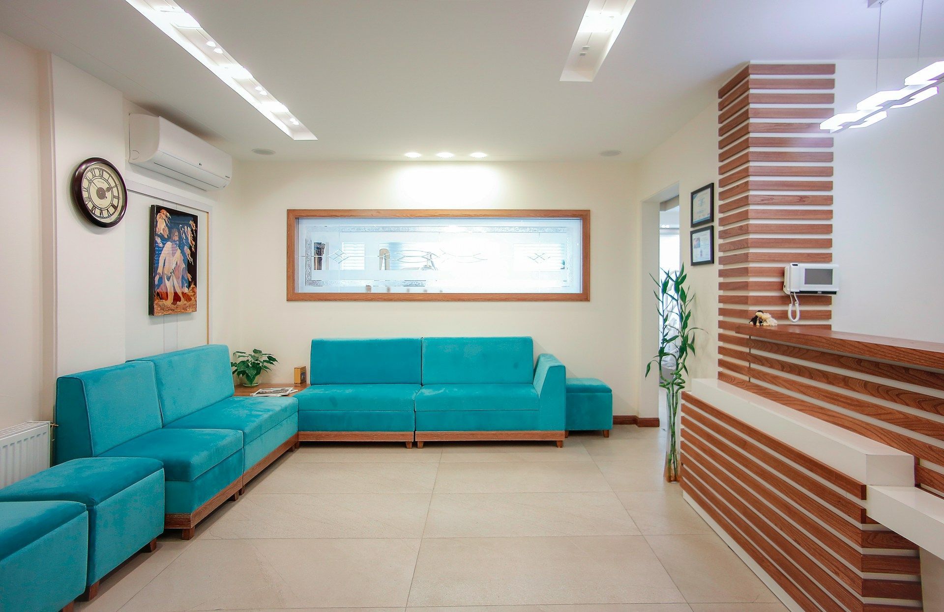 A waiting room with teal sofas, a wooden framed art, and a reception desk with brick pattern.