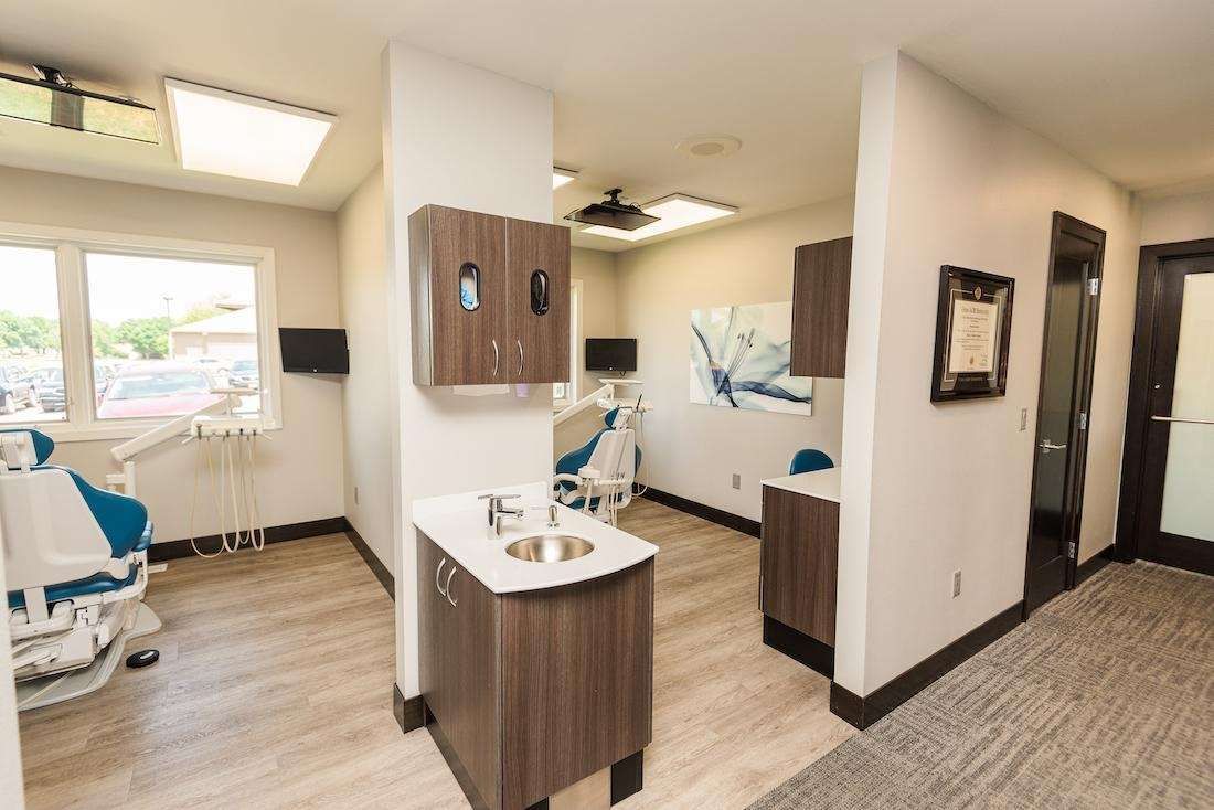 Dental office with examination rooms. Light wood floors, dental chair, cabinets, sink.