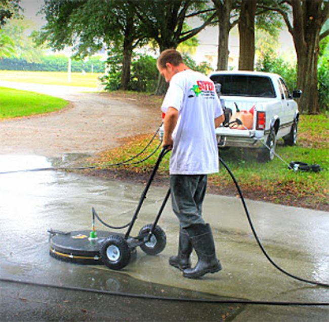 A man is using a machine to clean a driveway with a truck in the background