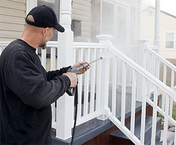 A man is cleaning a porch railing with a high pressure washer
