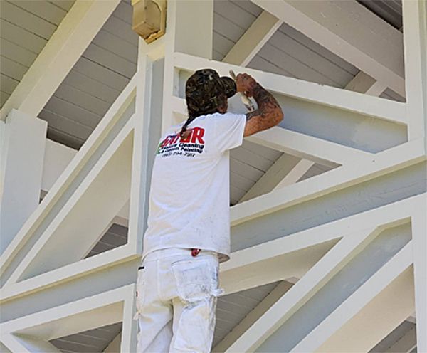 A man in a white shirt with the word hr on the back is painting a building