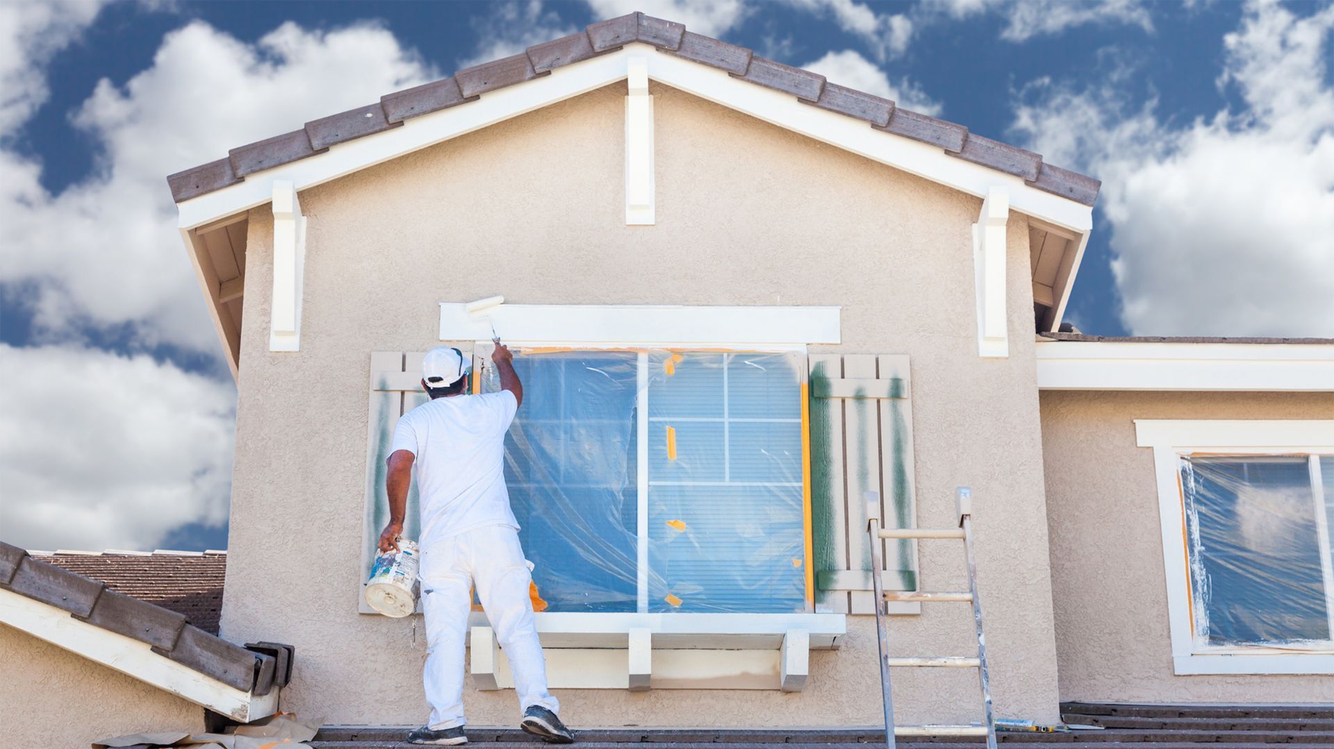A man is painting a window on the side of a house.