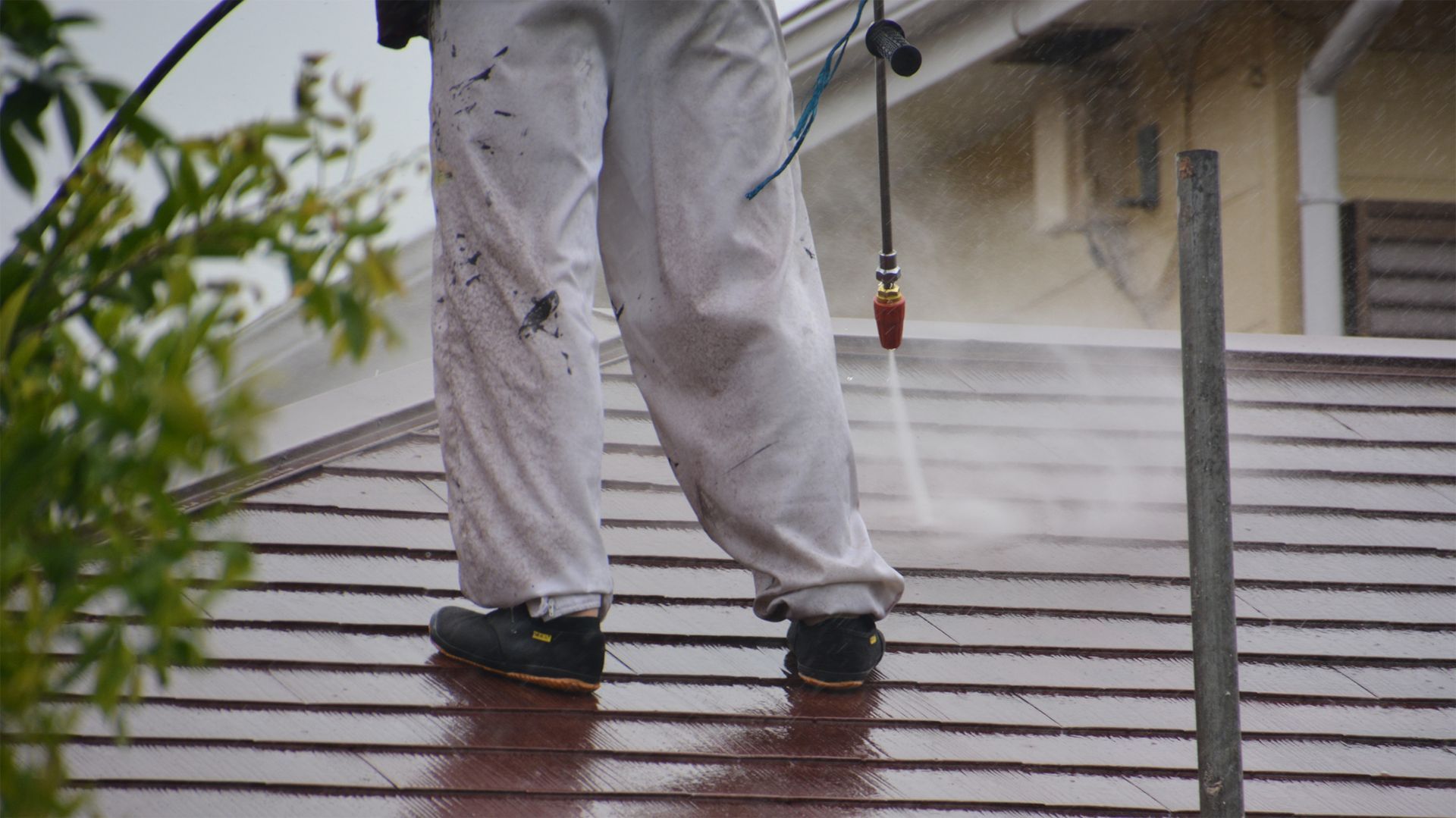A man is cleaning the roof of a house with a high pressure washer.