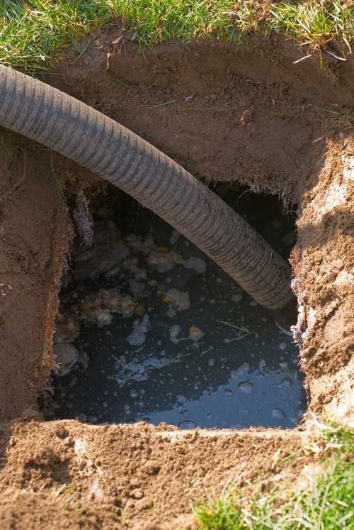 A hose drains murky water from a square hole in the ground.