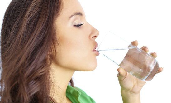 Woman in profile drinking water from a clear glass against a white background