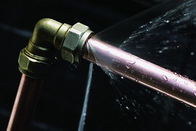 A metal pipe spraying water from a joint against a dark background