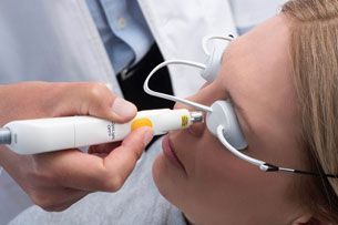 A person receives a dermatological laser treatment on their nose while wearing protective eye goggles.