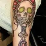 Skull tattoo with green eyes and floral details on a forearm