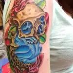 Colorful skull tattoo with blue, red, and tan shading on a person's forearm