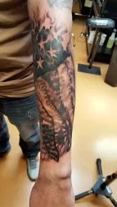 Tattooed forearm and hand extended downward, showing a star and winged tattoo in a room.