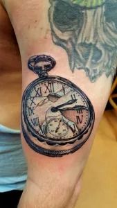 Black pocket watch tattoo on a lower leg, showing a compass-style clock face with Roman numerals.