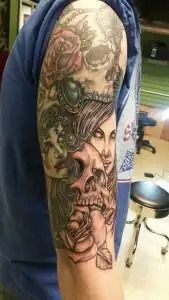 Detailed black-and-gray tattoo sleeve featuring a skull and surreal face on a person’s upper arm