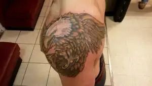 Close-up of a large lion tattoo on a person’s upper arm in a tiled indoor setting