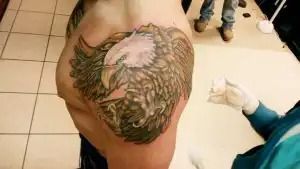 Person with a large bird tattoo on their shoulder in a tiled room, viewed from above.