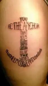 Tattoo on skin reading “Be the anchor that keeps me grounded in this crazy world,” with anchor design