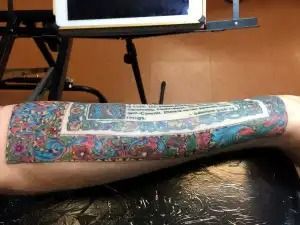 Tattooed forearm resting on a table, showing a colorful geometric sleeve design.