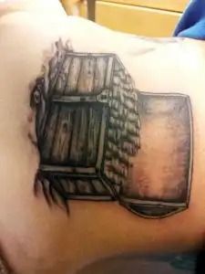 Black-and-gray tattoo of a rustic wooden chest on skin, with shaded panels and a hinged lid