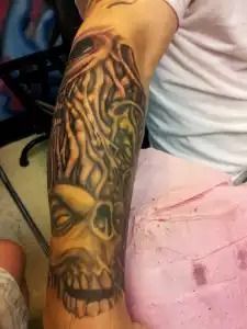 Arm tattoo sleeve featuring a detailed skull and swirling black-and-yellow tribal design