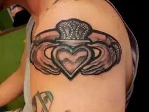Black tattoo of a winged heart and crown on a person's upper arm