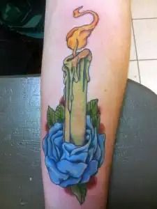 Tattoo of a lit candle with wax drips, wrapped in a blue rose and green leaves