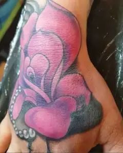 Pink and black floral tattoo on a person's arm, featuring large petal shapes and bead-like accents