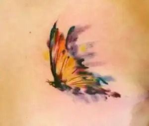 Colorful butterfly tattoo on skin with orange, purple, green, and black wings