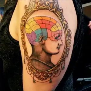 Colorful side-profile tattoo portrait in an ornate oval frame on an upper arm