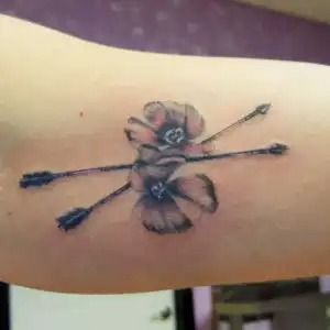 Rose tattoo with crossed arrows on a forearm, in black and gray ink