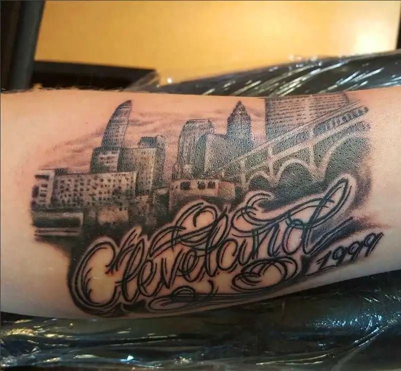 Black-and-gray forearm tattoo of a city skyline with script reading “Cleveland” and “1944”